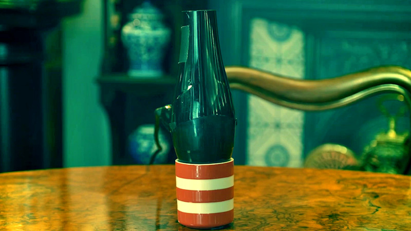 A black hairdryer is resting in a white and red coffee mug on a table in the Taskmaster house living room. A black hairdryer is resting in a white and red coffee mug on a table in the Taskmaster house living room.