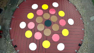 A shot from the top of the geodesic dome showing the floor. On the floor are 25 coloured circles in black, brown, red, yellow, and white arranged in a symmetrical pattern.