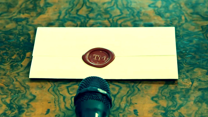 A sealed task resting on a marbled wooden table. In front of the task is a microphone. A sealed task resting on a marbled wooden table. In front of the task is a microphone.