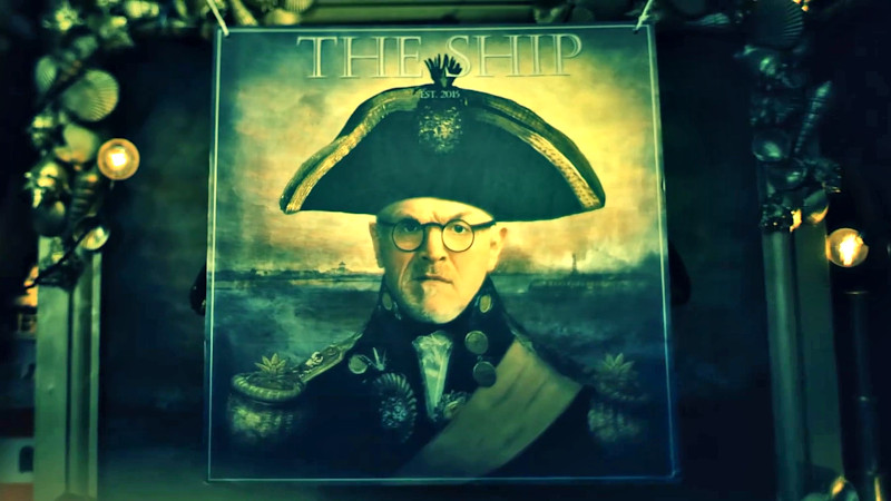 The Taskmaster's portrait with the words 'The Ship' printed on top, being suspended by string over the actual portrait. The Taskmaster's portrait with the words 'The Ship' printed on top, being suspended by string over the actual portrait.